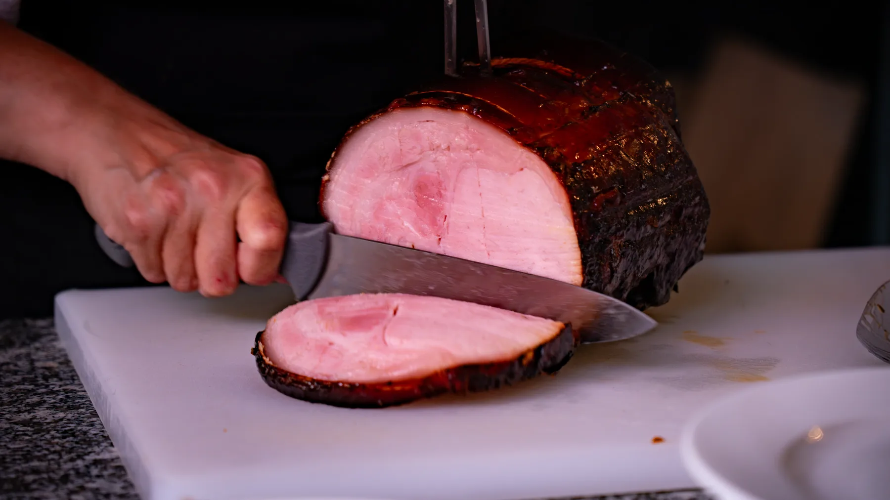 Découpe au couteau d'un jambon braisé caramélisé sur une planche